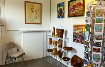 A white room with paintings on the wall, wooden crafts on shelves and cards on a card rack