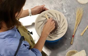 Image of a lady painting a plate with the Hakeme Brushwork