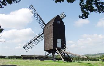 a windmill sitting on grass, looking out towards the hills