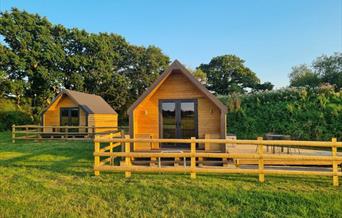 Two wooden cabins in a field with trees in the background
