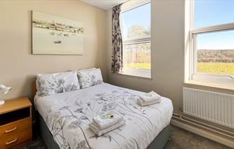 bed with towels on, with window looking out onto a field. Art work at the head of the bed
