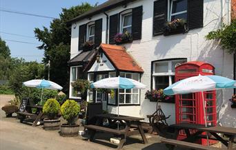 A photo of the outside of the Yew Tree Inn, there are wooden benches with parasols over them along the front of the pub.