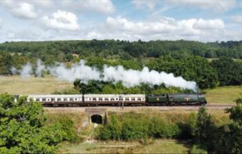A vintage steam train driving on a railway bridge through the High Weald countryside