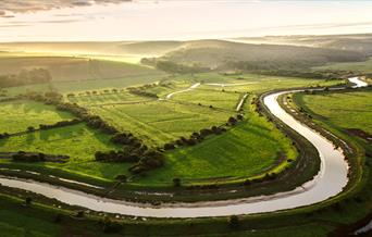 winding river with green fields and dappled sunshine