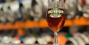 A glass of ale with kegs in the background