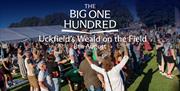Crowd gathered at an outdoor event with tents and stalls, with “The Big One Hundred – Uckfield’s Weald on the Field 8th August” text overlaid.