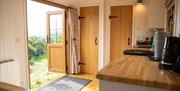 Interior of a shepherds hut; with a kitchen side and sink, two doors leading to bedrooms/bathroom, and a front door looking out onto the field