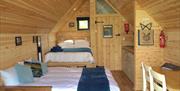 A wooden cabin with a double bed and a double sofa bed, with a small kitchen and table and chairs on the side