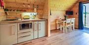 A wooden cabin with a small cream kitchen, with an oven, sink, kettle and toaster. Chairs and table in the background