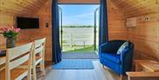 A wooden cabin with the double doors opening onto a field, with an armchairs, two wooden chairs and table inside the cabin