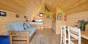 A wooden cabin with a sofa, table and chairs, with a bed in the background