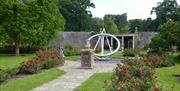 A garden with rose bushes and a sun dial in the middle of the pathway