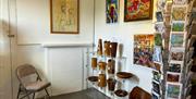 A white room with paintings on the wall, wooden crafts on shelves and cards on a card rack