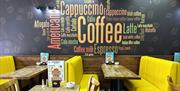 Interior of Aroma Café with yellow booth seating and large coffee-themed wall mural featuring words like cappuccino, espresso and latte