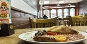Traditional full English breakfast with sausage, fried egg, beans, mushrooms, hash brown and toast served on a wooden table inside Aroma Café