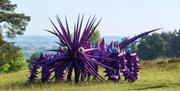 A group of performers operate a large, purple, many-legged creature with long spikes and eye-like features, moving across an open grassy hillside with