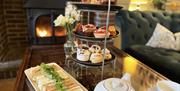 An image of a stacked cake stand on a table beside a plate of sandwiches, a pot of tea and a cup and saucer.