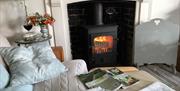 A sofa with pillows and a book on it with a lit log burner in the fireplace.