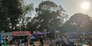 Visitors relaxing in a festival arena at One Love Festival, with food stalls, seating areas and open green space in the afternoon sunshine.