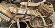A selection of heritage baskets outside on top of a wooden table. Some are traditional Sussex trugs and others are woven baskets