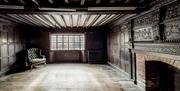 An old room with dark wood panelling, and a fireplace. Empty except for a green armchair in the corner