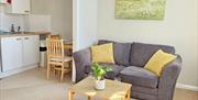 A living area with a couch and a coffee table. On the left is part of the kitchen, with a sink and table and chairs