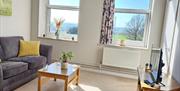 A living area, with a couch, coffee table and TV and stand. Two single windows look out over a field