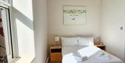 A bedroom with a double bed and two bedside tables. Artwork hangs on the wall above the head of the bed, and towels are placed on the bed