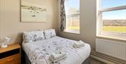 bed with towels on, with window looking out onto a field. Art work at the head of the bed
