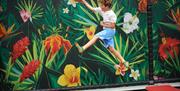 Visitor bouncing on a trampoline at Go Wild! in Heathfield, reaching for a ball against a vibrant jungle-themed wall mural.