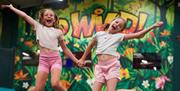 Two children jumping on trampolines at Go Wild! in Heathfield, with colourful rainforest artwork and Go Wild! branding in the background.