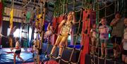 Visitors navigating a rope climbing course at Go Wild! in Heathfield, featuring soft play obstacles, climbing nets and adventure activities indoors.