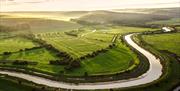 winding river with green fields and dappled sunshine