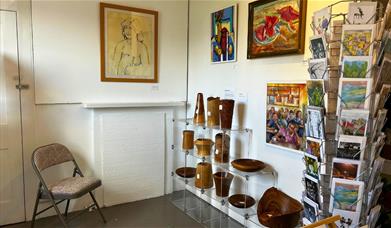 A white room with paintings on the wall, wooden crafts on shelves and cards on a card rack