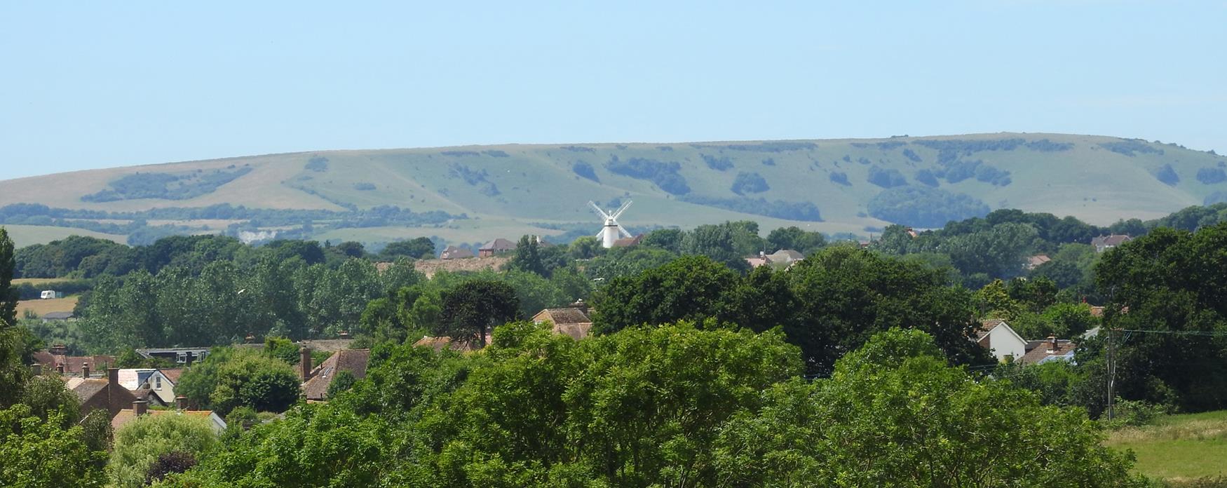 polegate windmill in the distance surrounded by green trees and rolling green fields