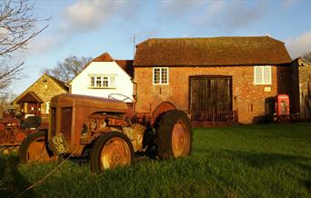 old style tractor in front of farmhouse with a red telephone box in front