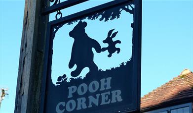 a black sign with the outline of winnie the pooh and piglet and the words pooh corner in gold