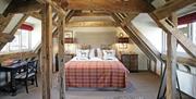 A bed in the centre of the room with sloping ceilings and dark beams.