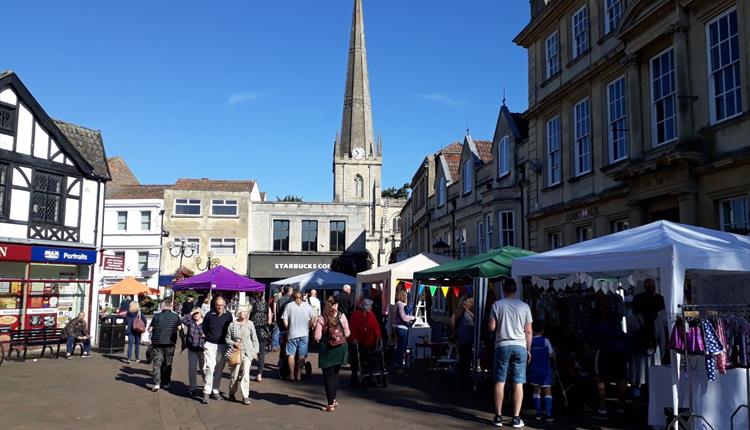 People looking around market with church spire in background