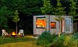A photo of one of the cabins surrounded by lush greenery and the woodland behind