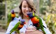 women feeding lorikeets, one on each hand and one on her shoulder