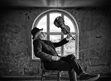 George seated in a room in front of a window holding a violin