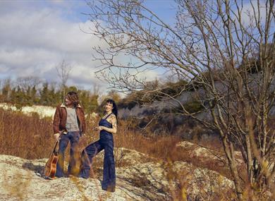 Hannah Sanders & Ben Savage 2025 - posed in nature with a guitar
