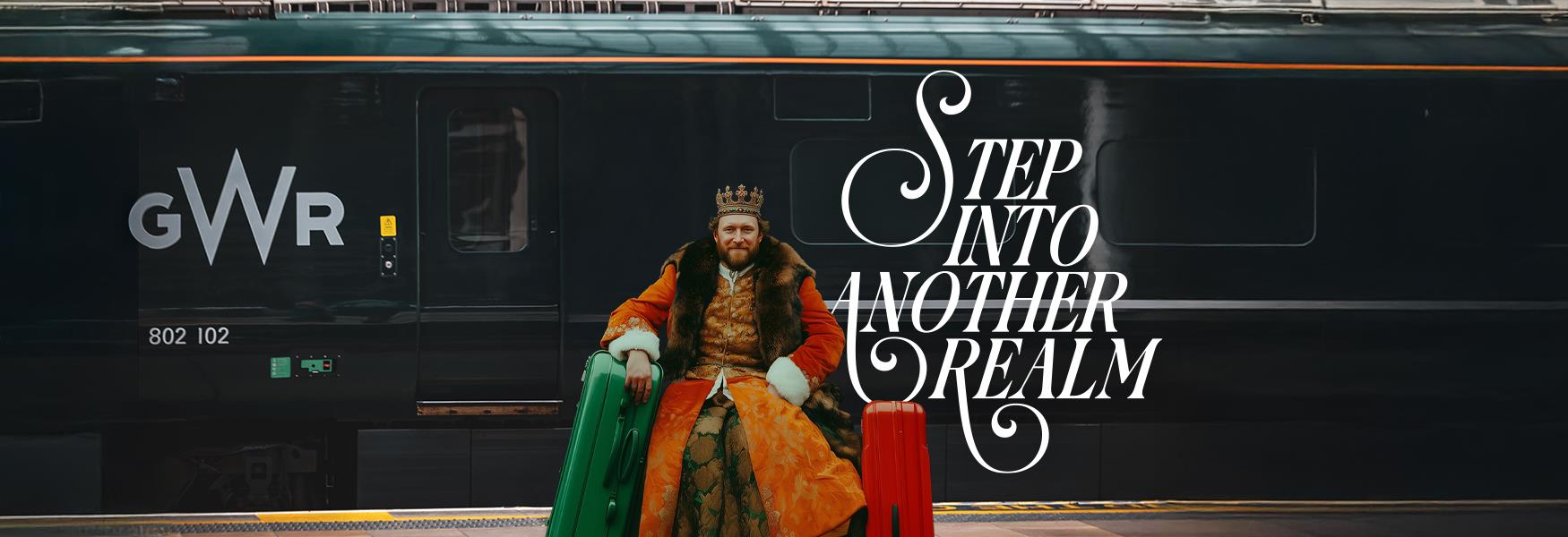 Person in Tudor dress sitting with luggage on a train platform with GWR train in the background