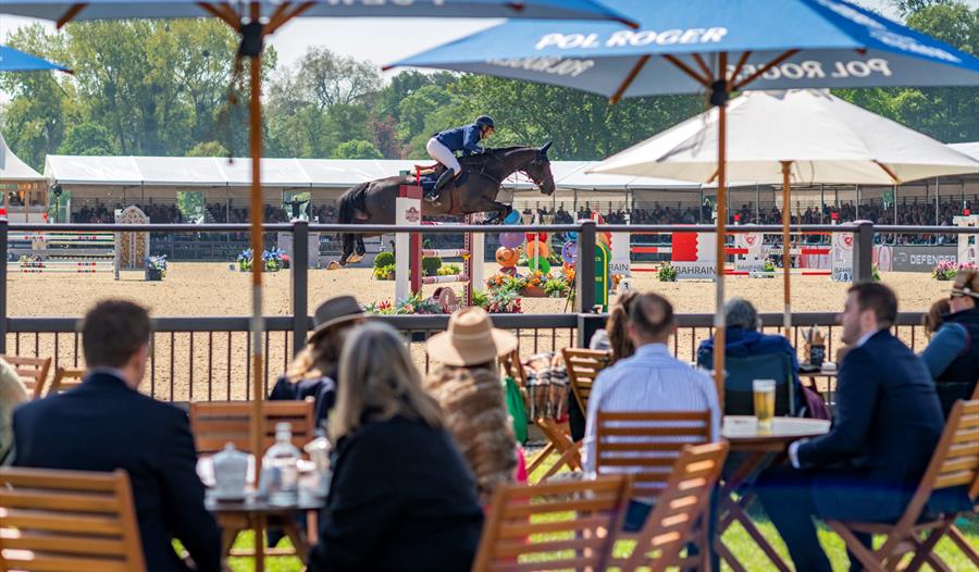 Royal Windsor Horse Show - people at tables under parasols watching showjumping