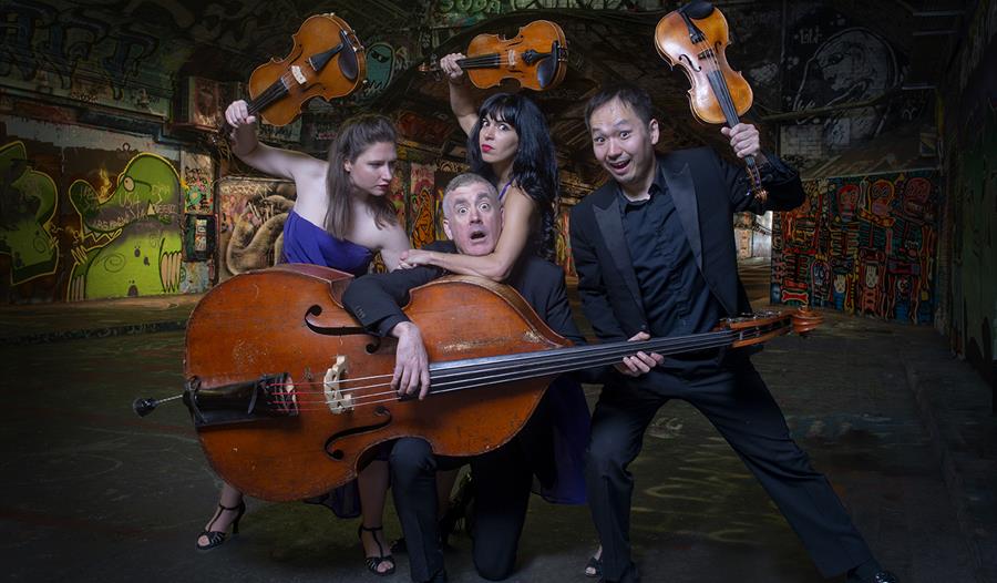 Graffiti Classics - formally dressed string quartet play fighting with their instruments in front of urban wall - ©David Pickens