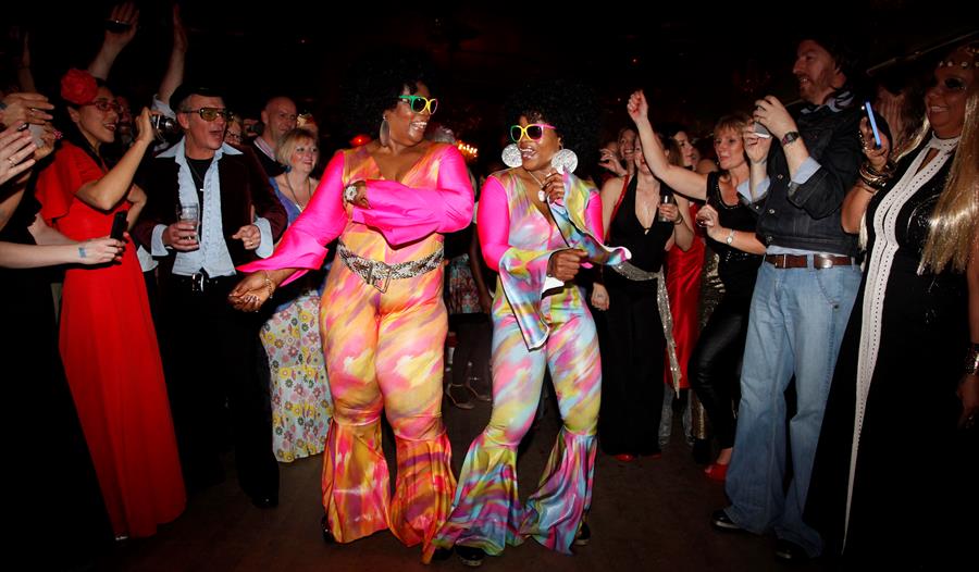 Haven’t Stopped Dancing Yet! - crowd dancing, two ladies in the middle wearing retro disco outfits