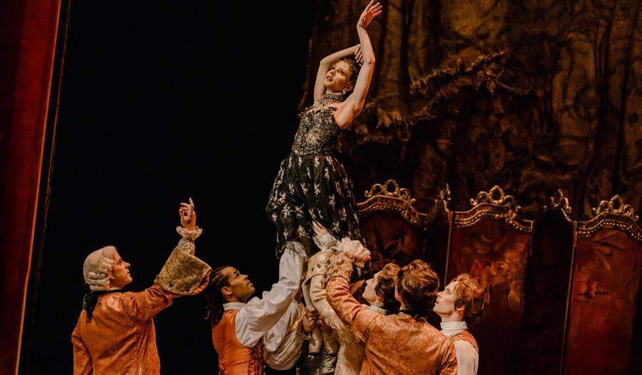 Manon - production shot - lady held up by a group of men in period dress