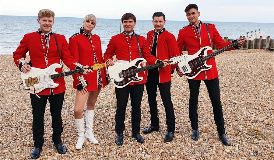 The Zoots on a beach in guardsmen tunics holding guitars