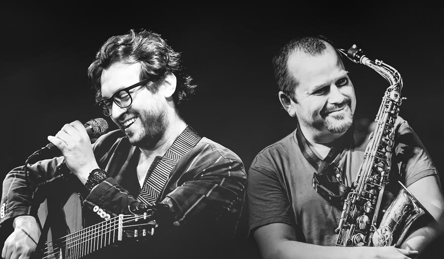 Tribute to Stan Getz & João Gilberto - black and white image of man with microphone and guitar and man hugging a saxophone